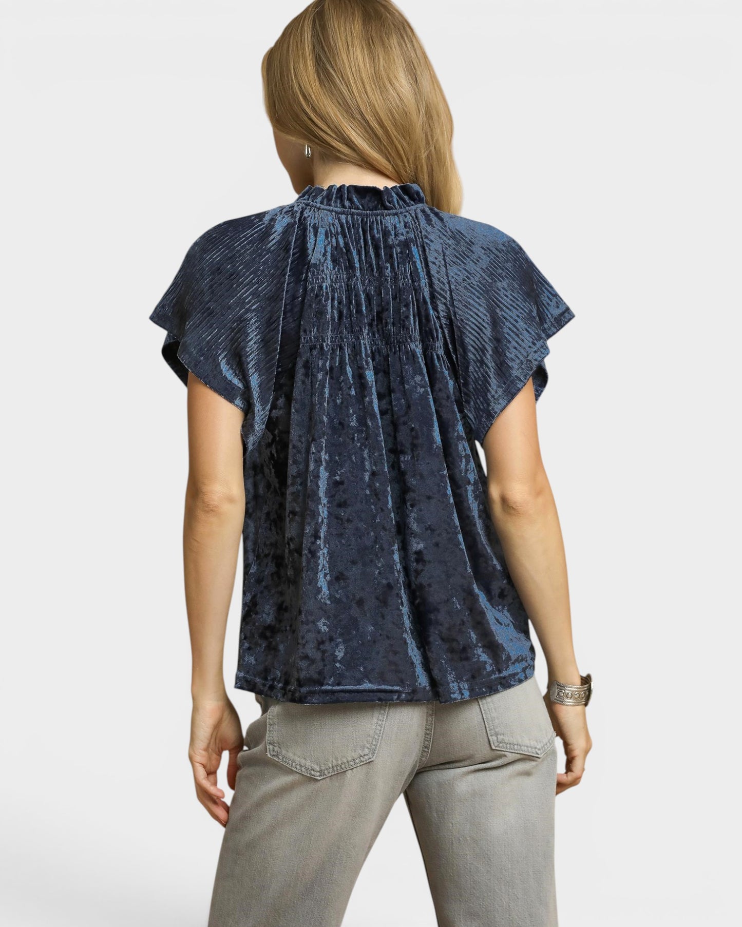 Woman wearing a blue patterned top and light gray pants on a white background