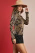 Woman wearing a patterned long-sleeve top and black shorts with a beige hat against a red and beige background.