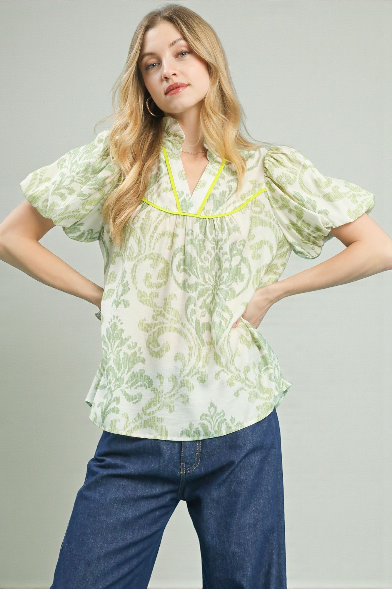 Woman wearing a floral blouse with short sleeves and blue jeans on a gray background