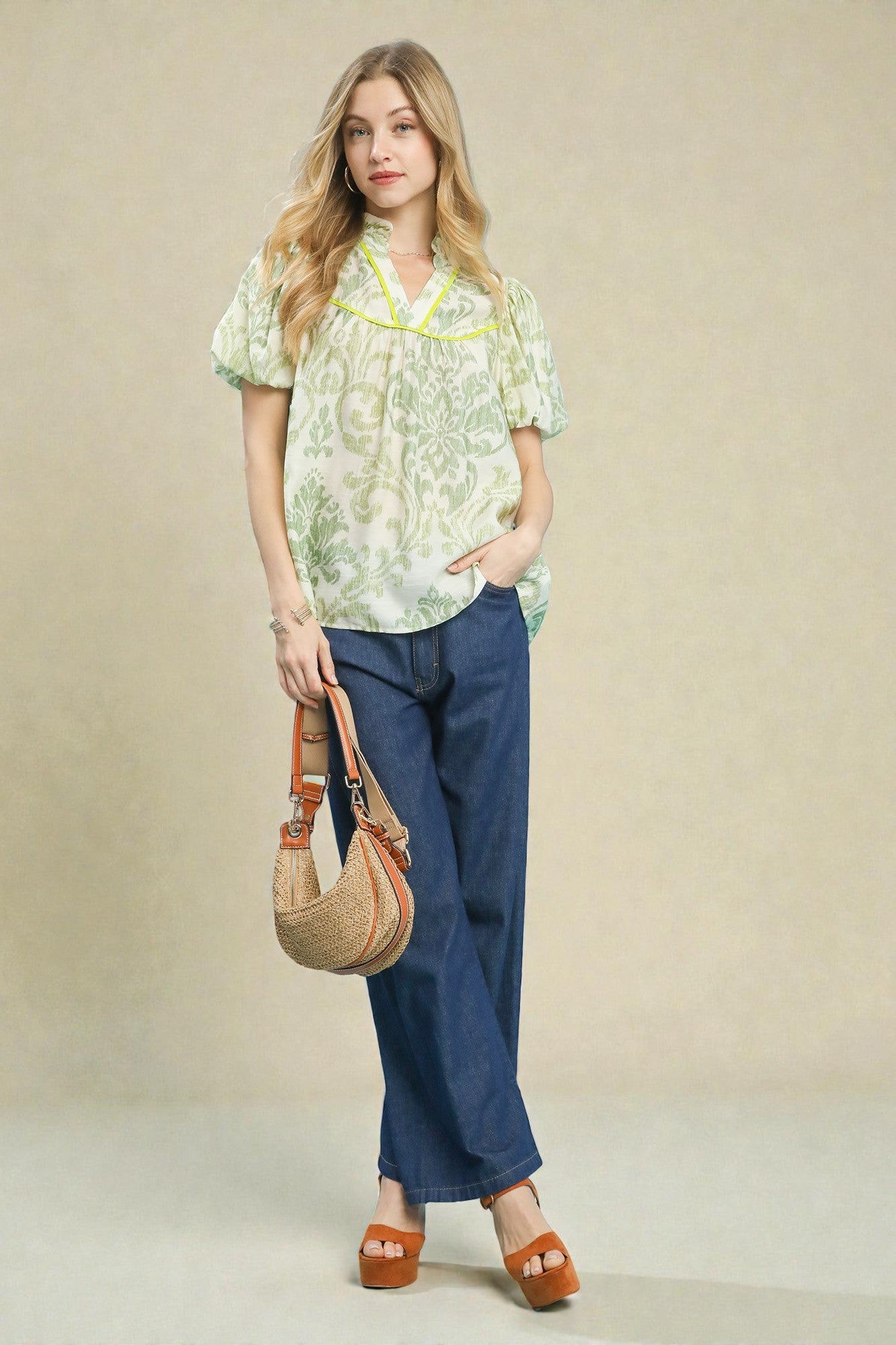 Woman wearing a floral blouse and blue jeans, holding a woven bag against a beige background