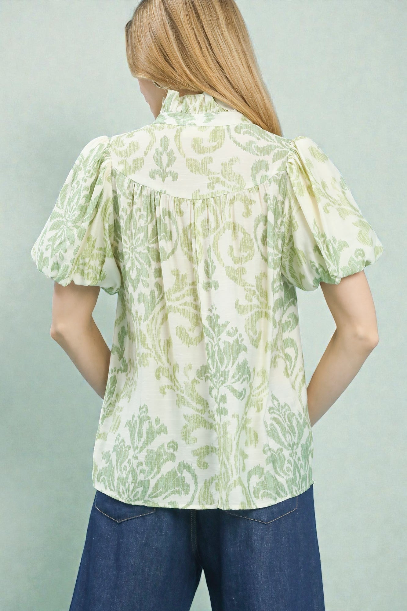 Woman wearing a light green floral blouse with short sleeves against a plain background