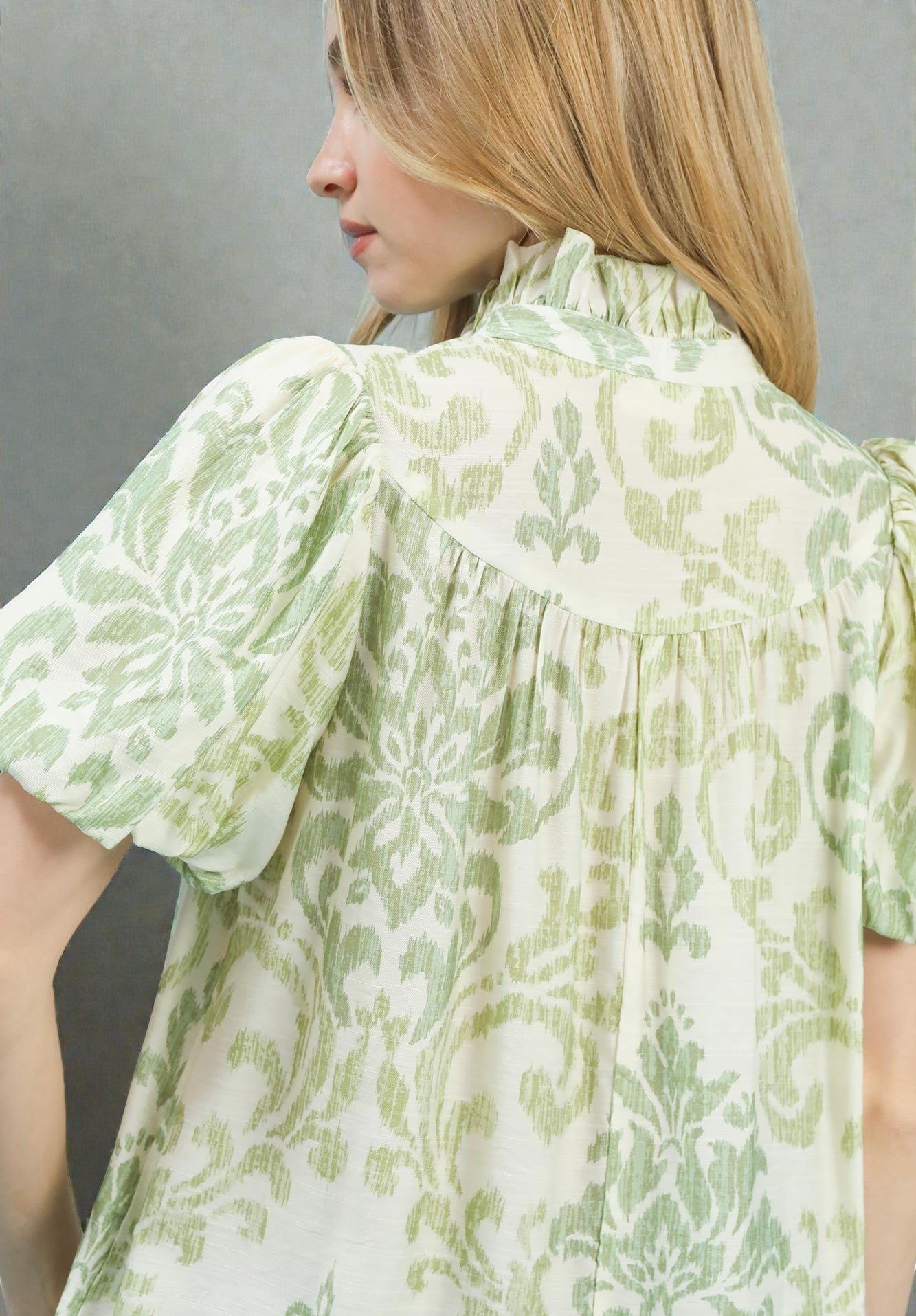 Woman wearing a green and white patterned blouse against a gray background