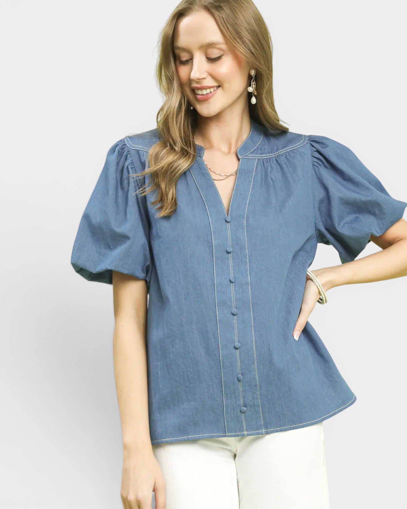 Woman wearing a blue denim blouse with white pants on a light gray background