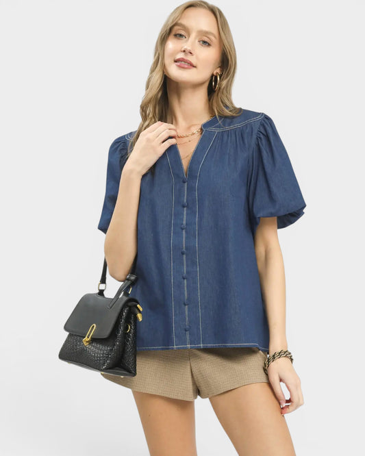 Woman wearing a blue blouse and beige shorts, holding a black handbag on a white background