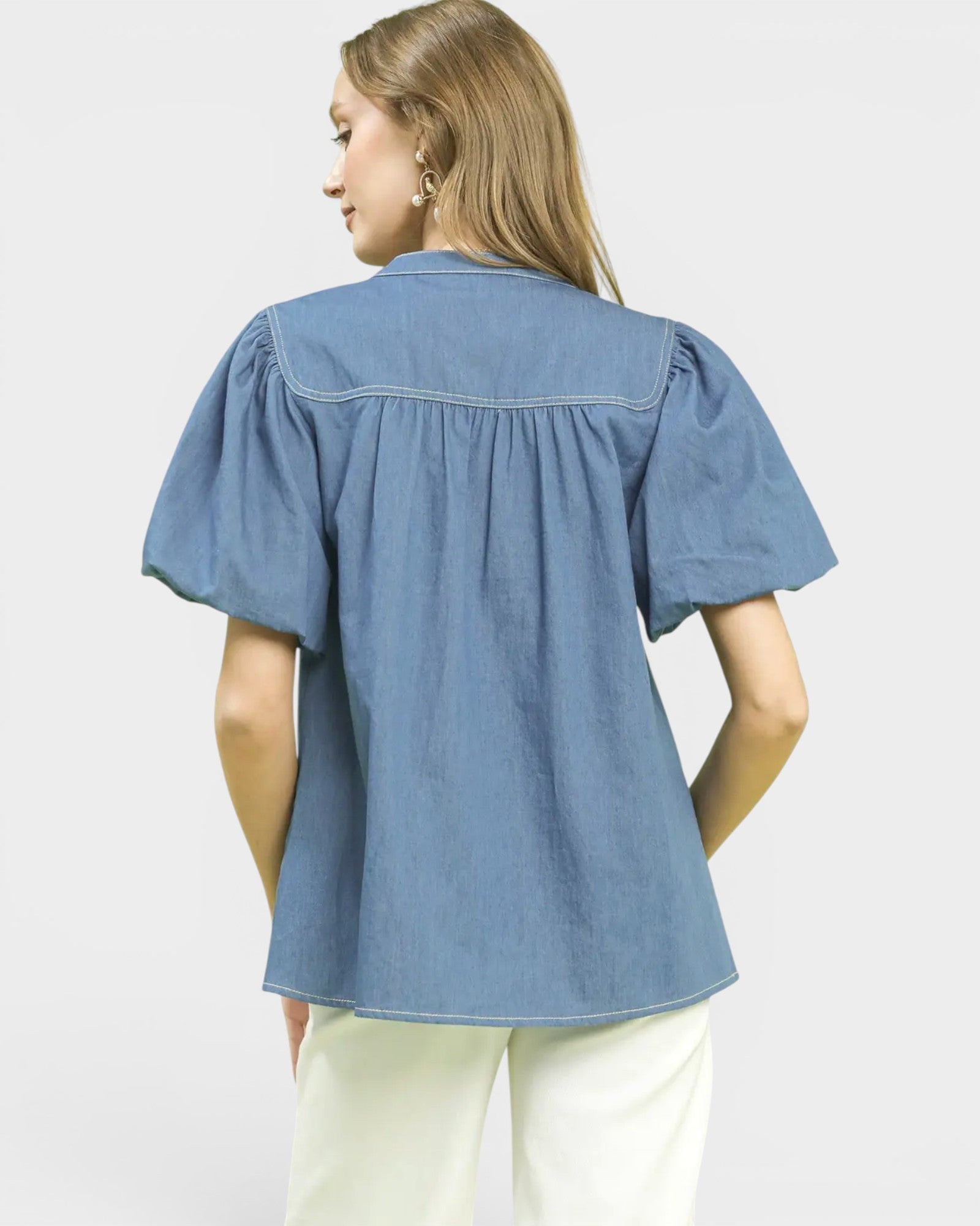 Woman wearing a blue denim blouse with puff sleeves on a light gray background
