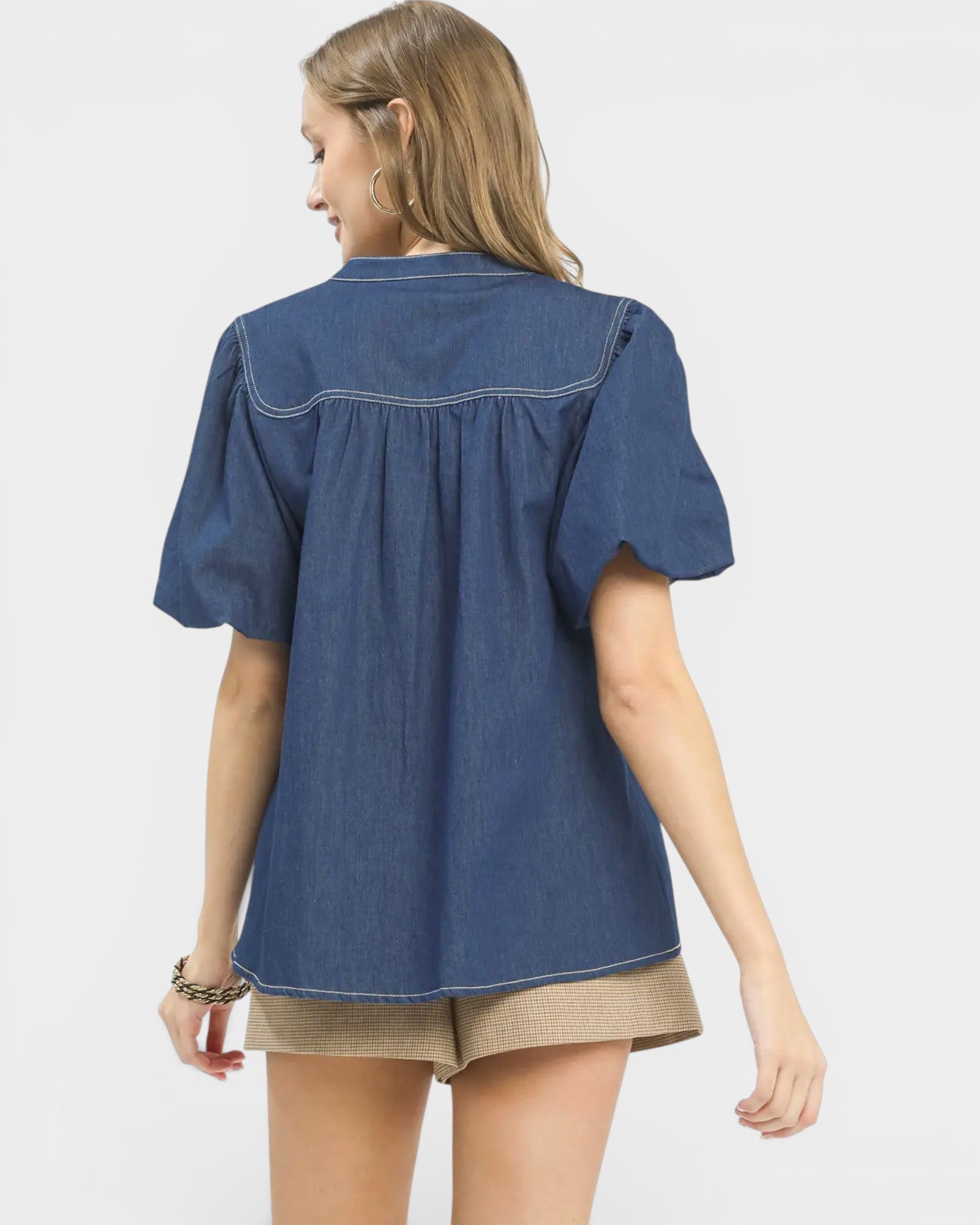 Woman wearing a blue denim shirt and beige shorts on a white background