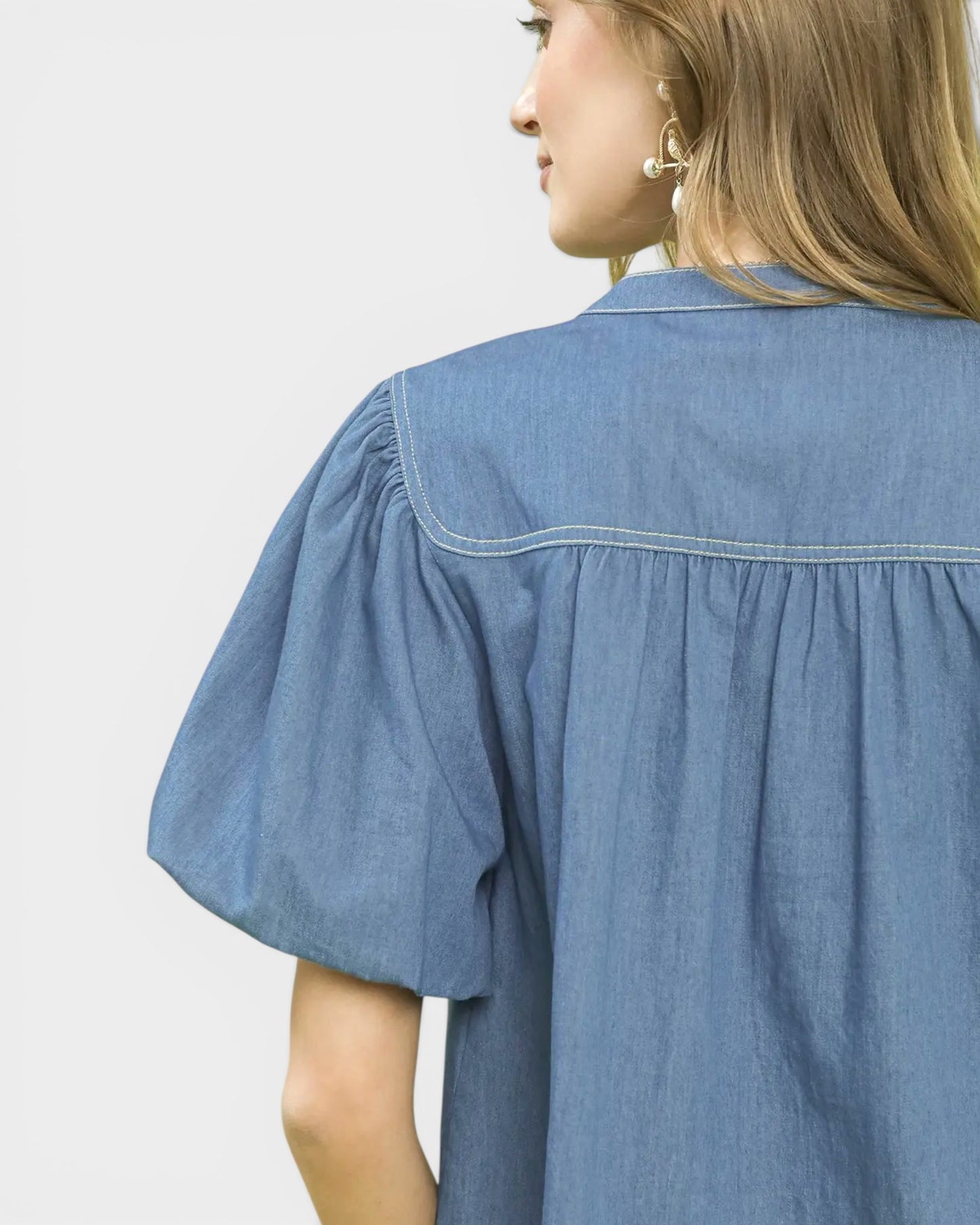 Person wearing a blue denim shirt against a plain background