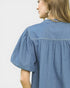 Person wearing a blue denim shirt against a plain background