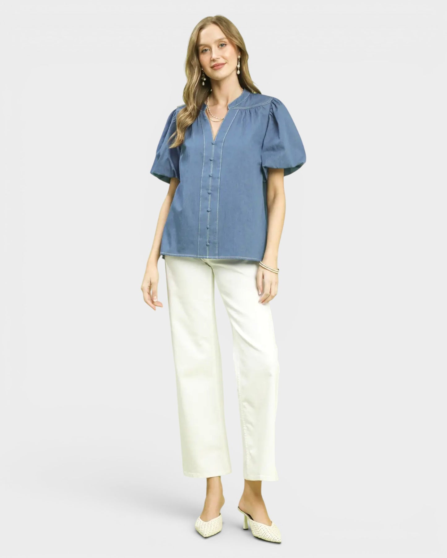 Woman wearing a blue blouse and white pants on a light gray background