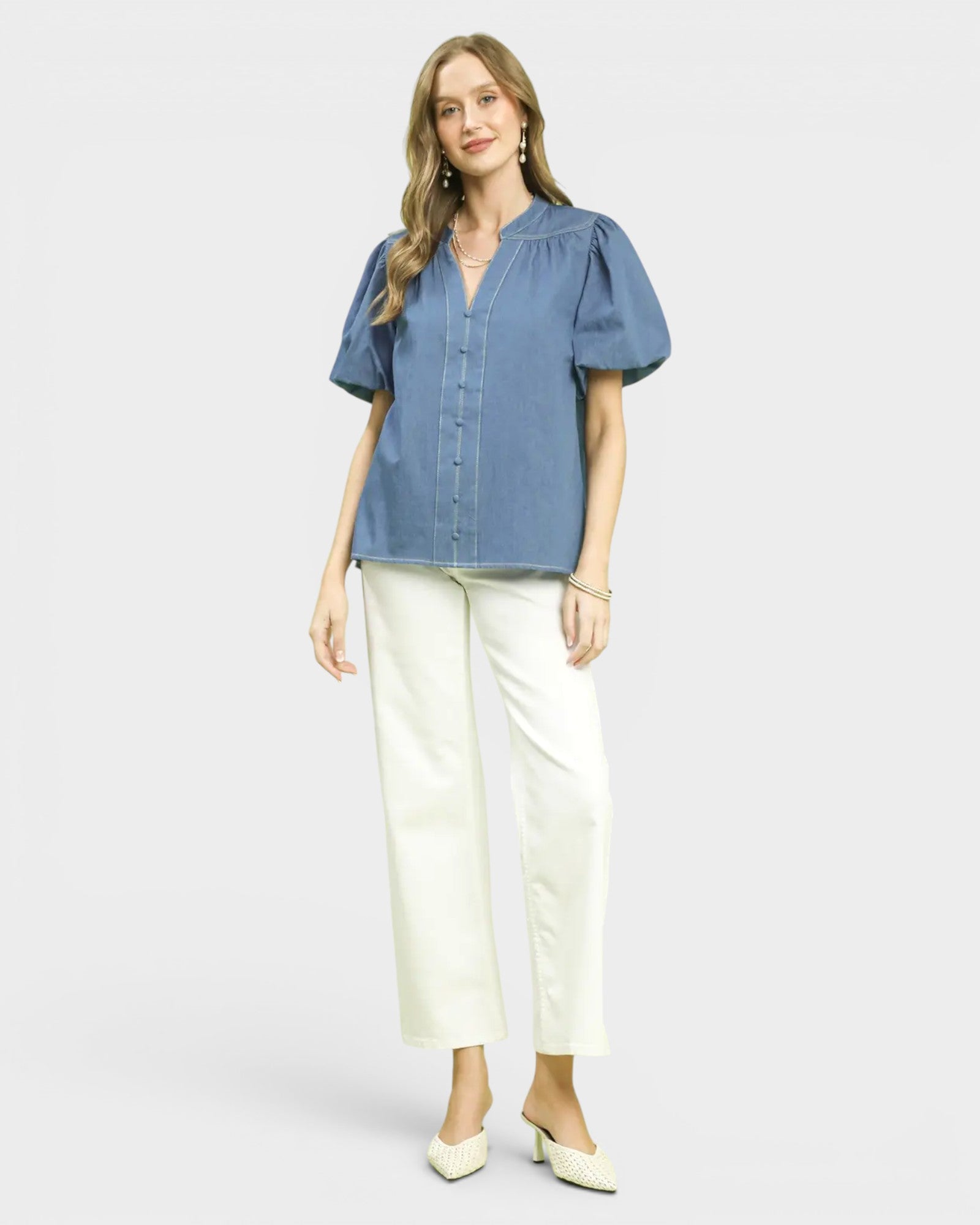 Woman wearing a blue blouse and white pants on a light gray background