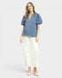 Woman wearing a blue blouse and white pants on a light gray background