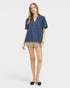 Woman wearing a blue denim shirt and beige shorts on a white background