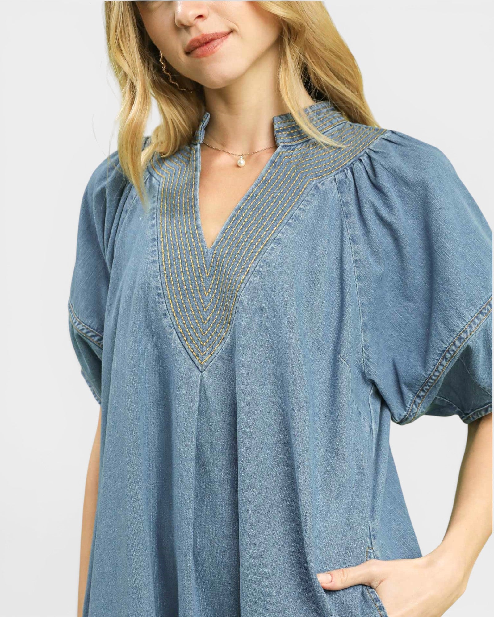 Woman wearing a blue denim dress with embroidered details on a light gray background