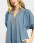Woman wearing a blue denim dress with embroidered details on a light gray background