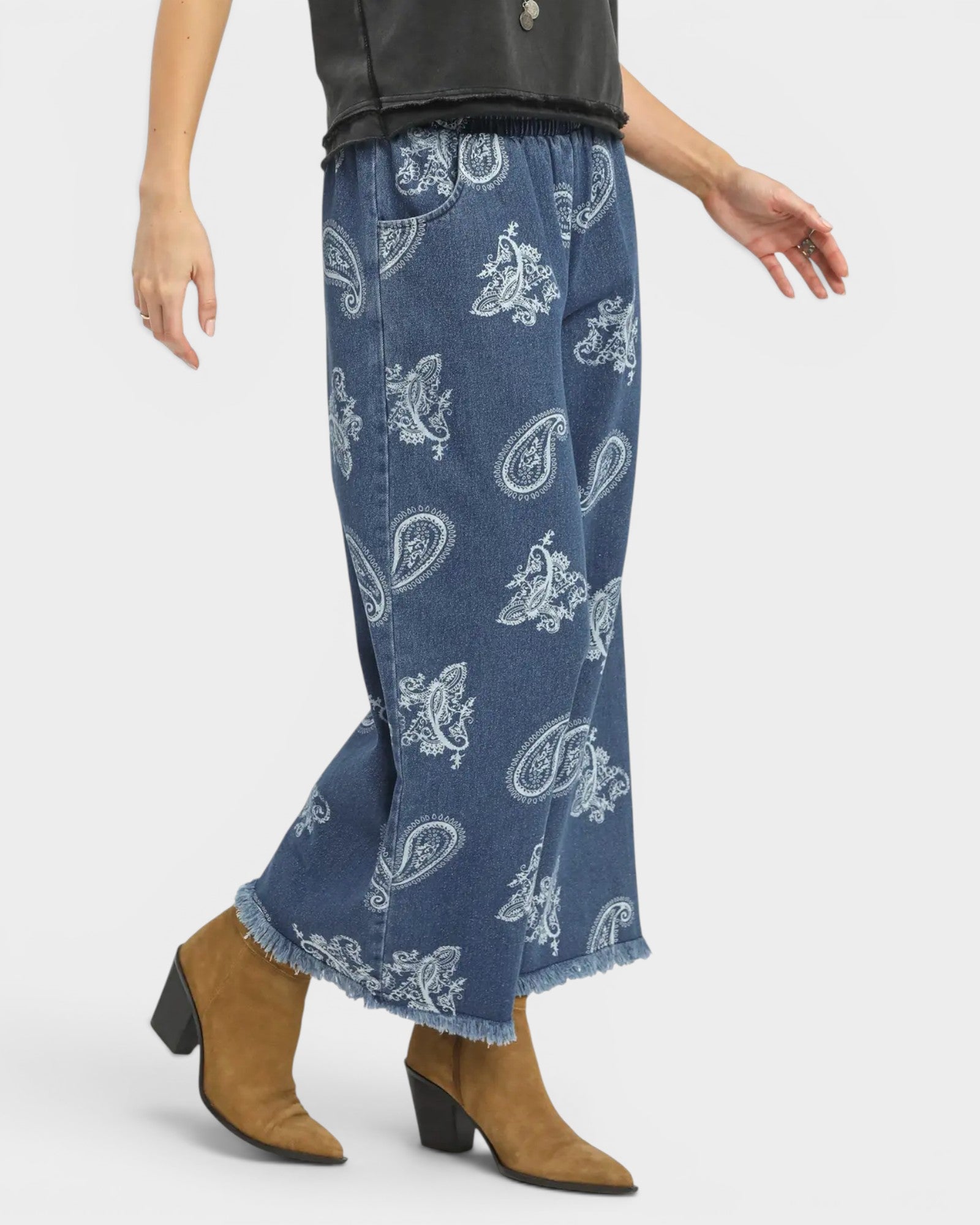 Person wearing blue paisley-patterned jeans with brown boots on a white background