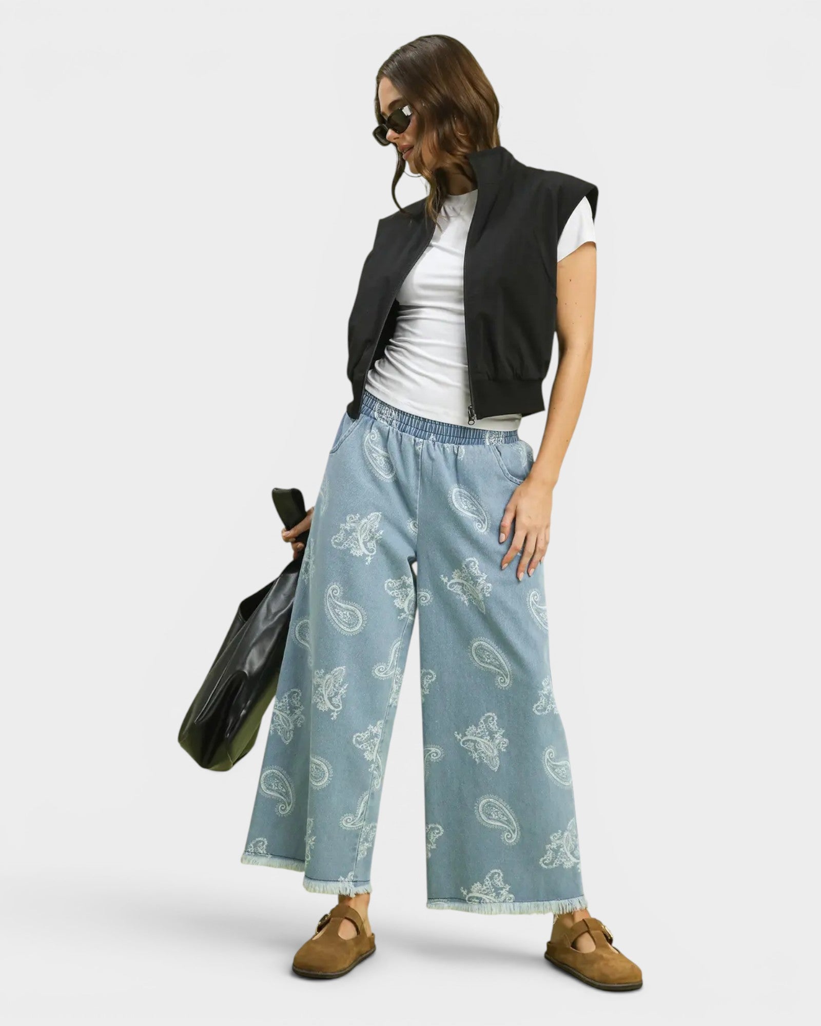 Woman wearing a black vest, white shirt, and blue patterned pants on a white background