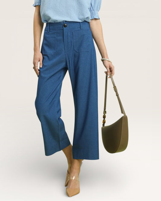 Person wearing blue pants and a light blue top, holding a green bag on a beige background