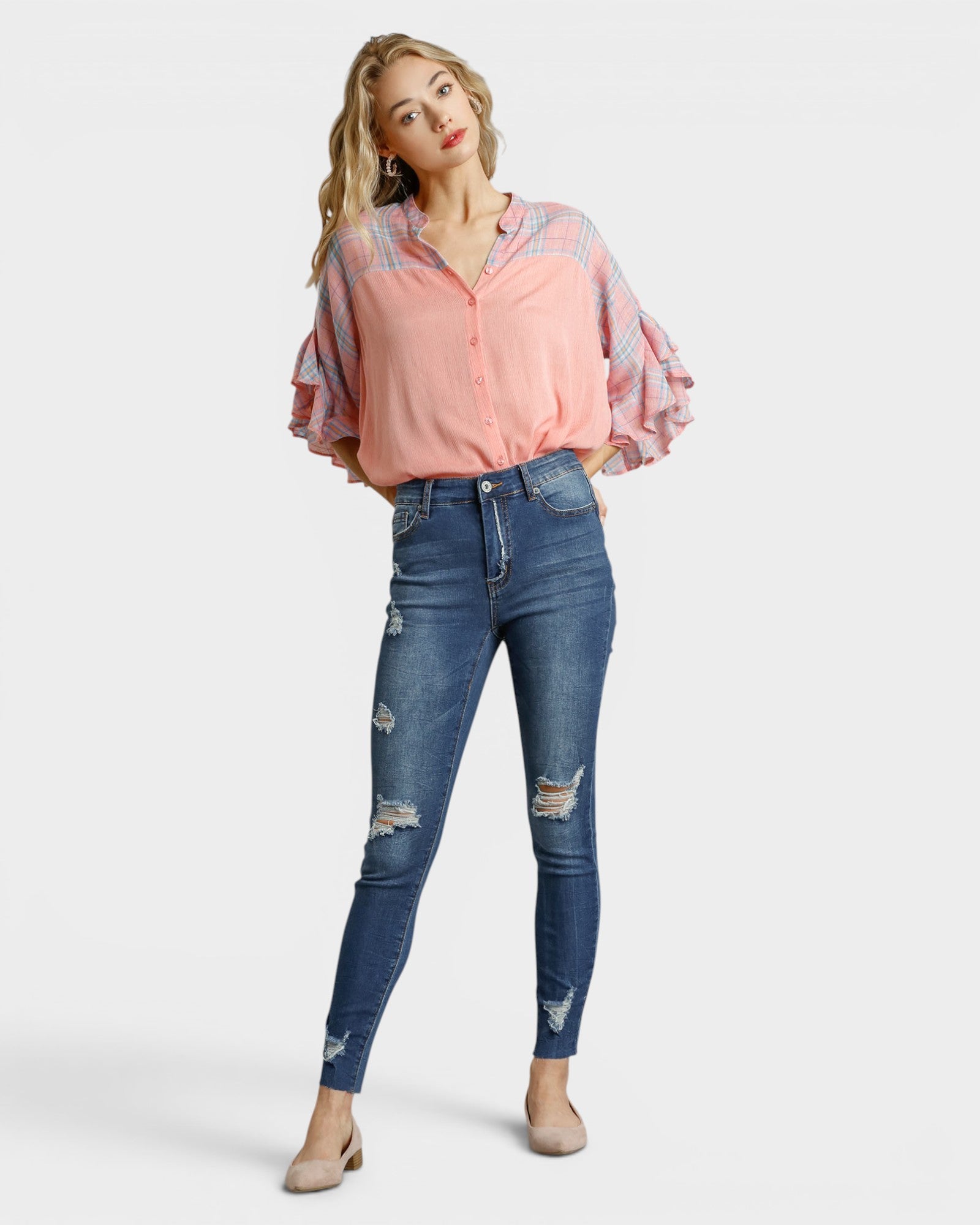 Woman wearing a pink blouse with ruffled sleeves and blue jeans on a white background