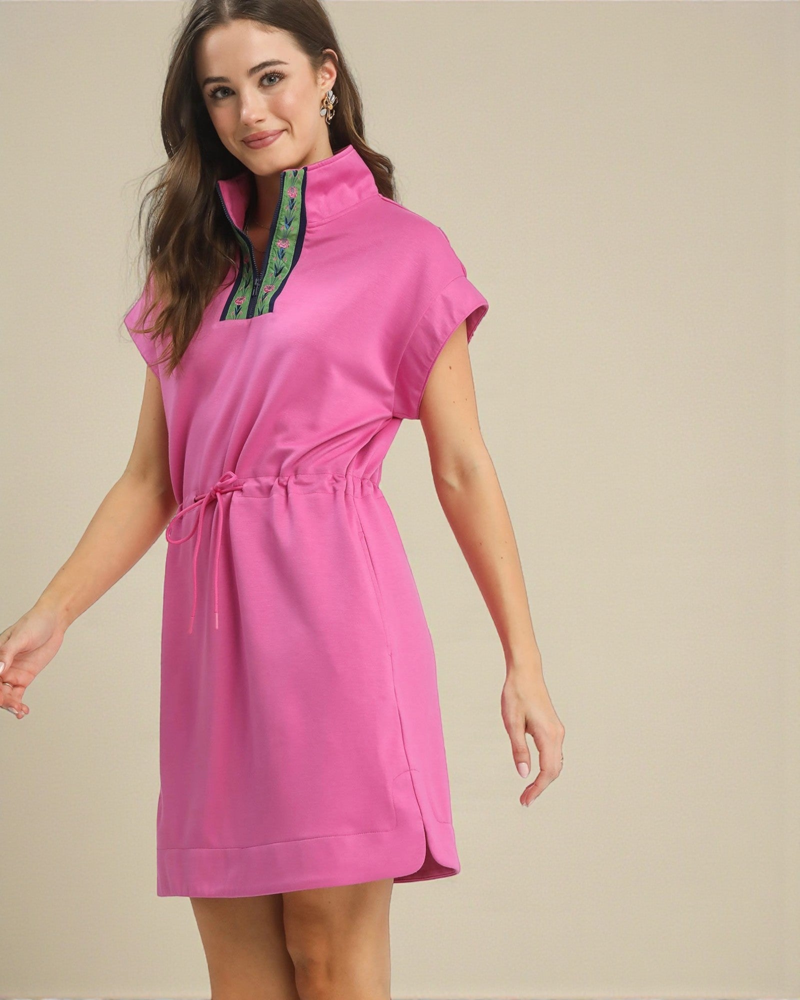 Woman wearing a pink dress with a green trim on a beige background