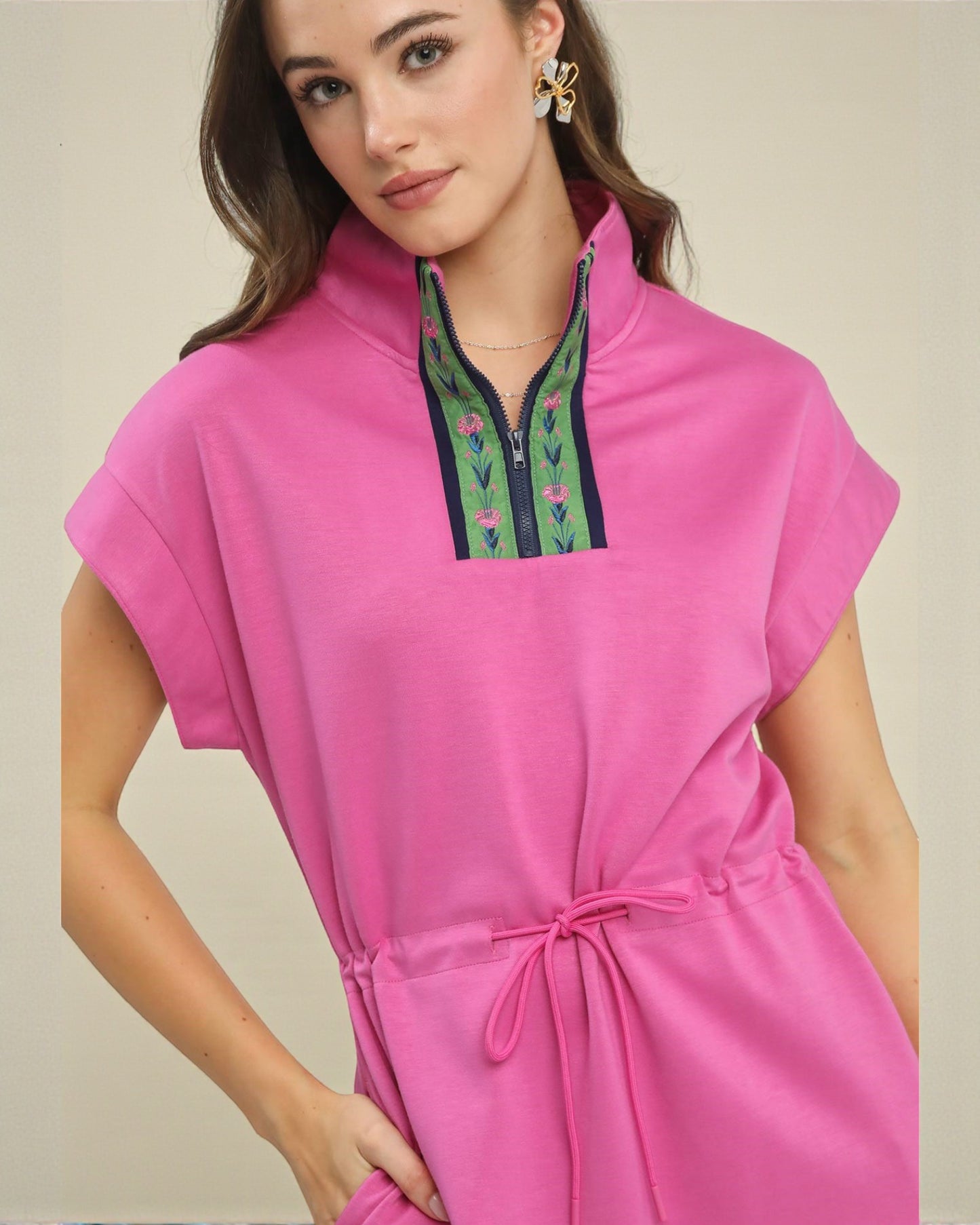 Woman wearing a pink dress with floral embroidery on a beige background