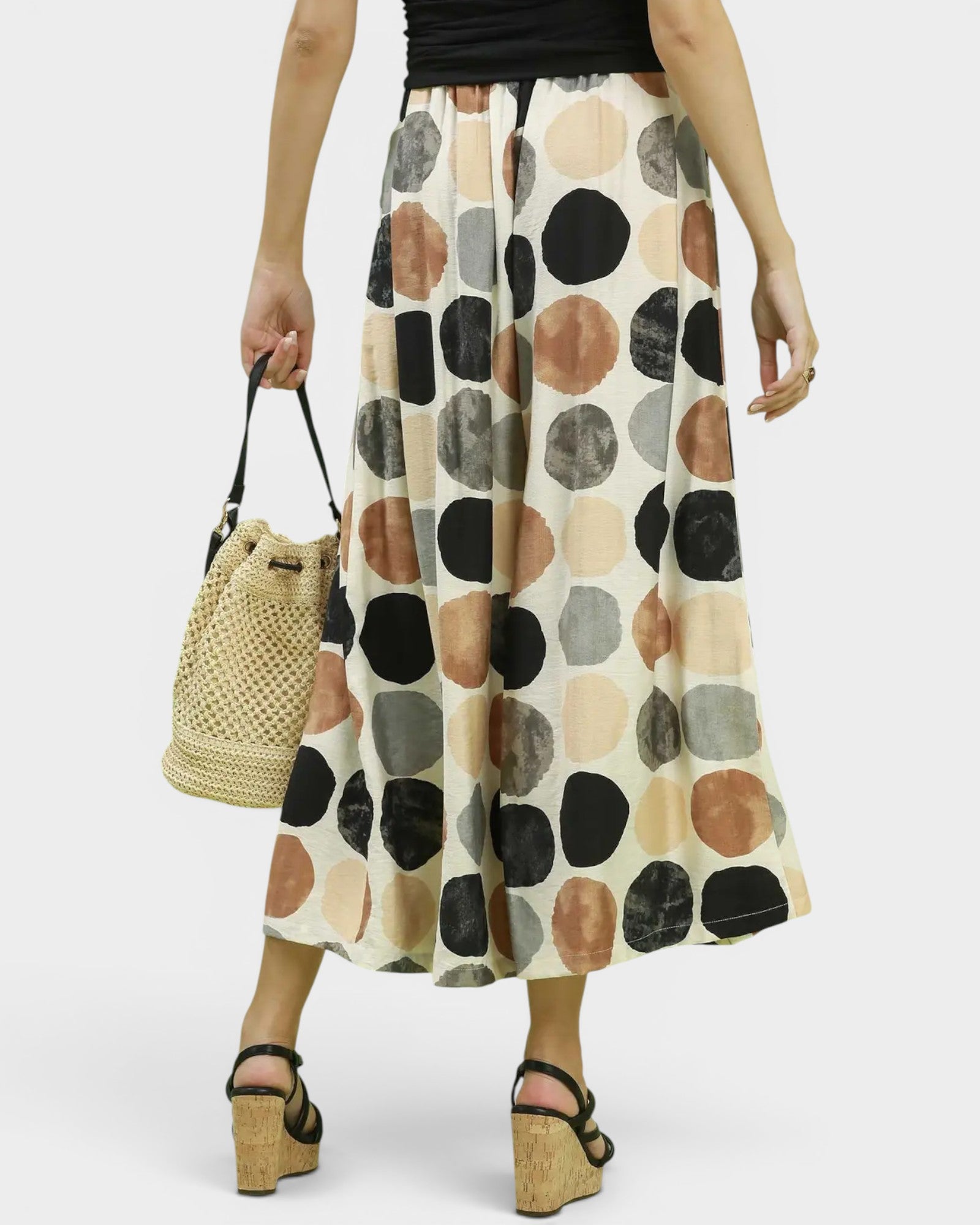 Person wearing patterned pants holding a straw bag on a white background