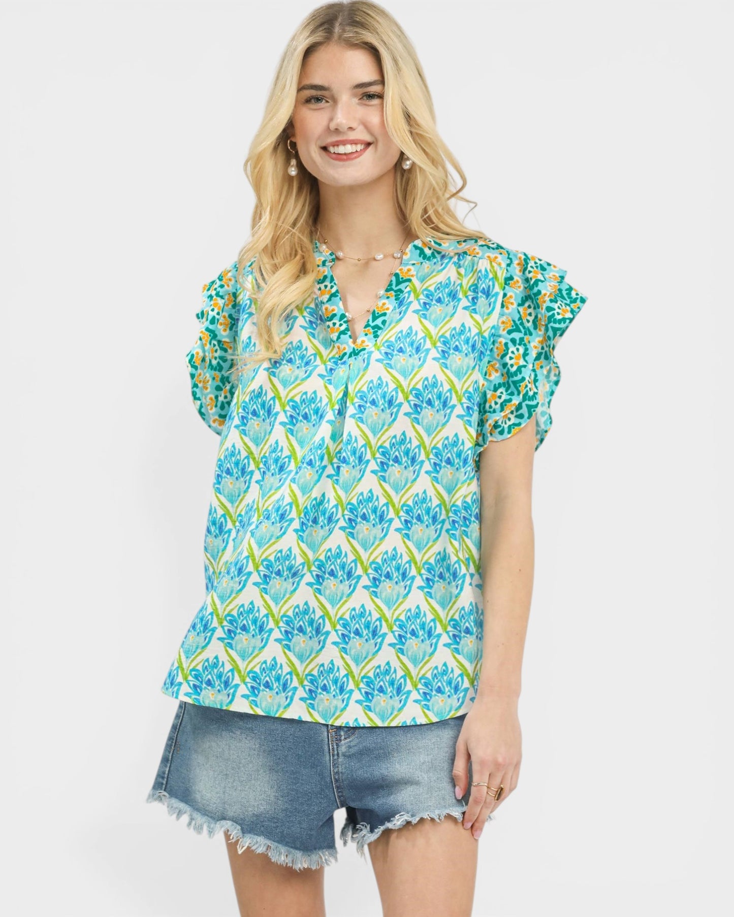 Woman wearing a blue and green floral blouse with denim shorts on a white background