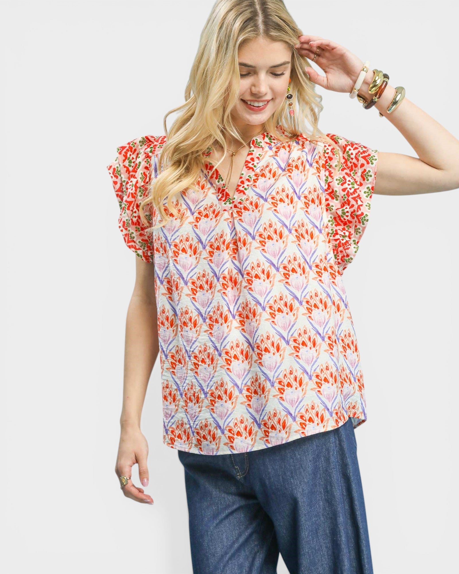 Woman wearing a colorful patterned top with blue pants on a white background
