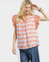 Woman wearing a colorful patterned top with blue pants on a white background