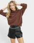 Woman wearing a brown sweater and black leather shorts on a white background