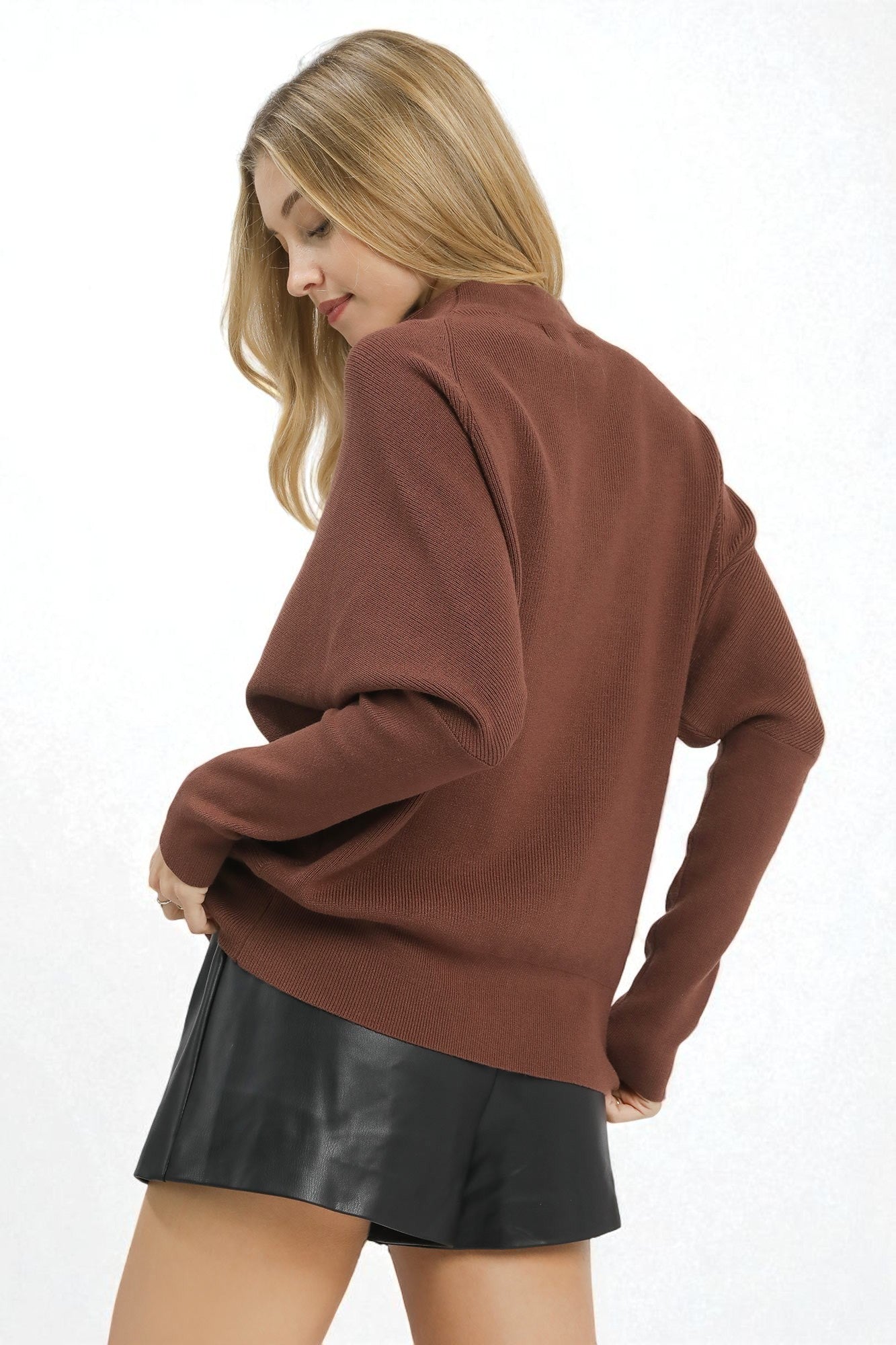 Woman wearing a brown sweater and black leather shorts on a white background