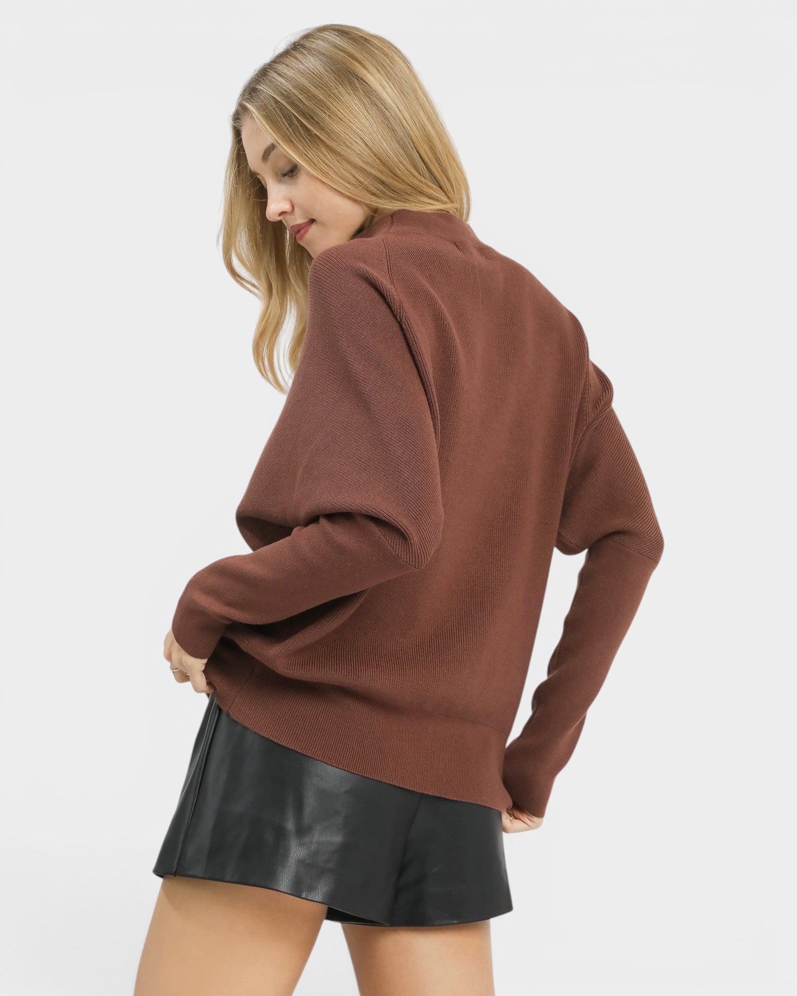 Woman wearing a brown sweater and black leather skirt on a white background