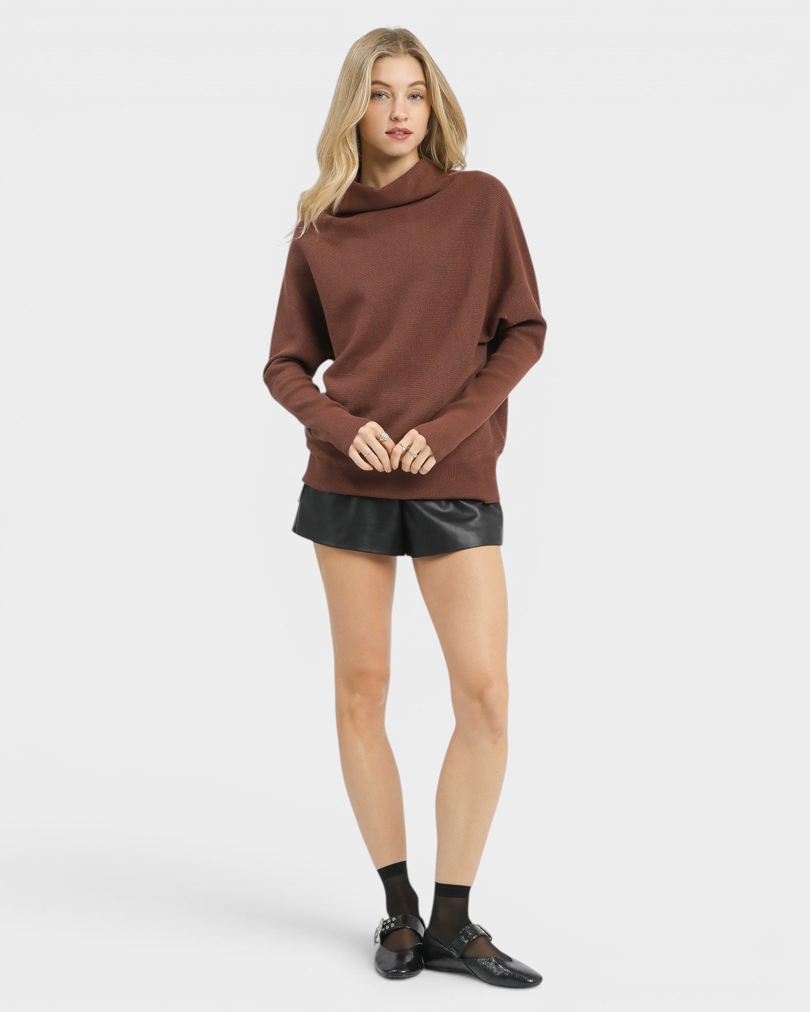 Woman wearing a brown sweater and black shorts on a white background