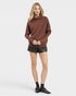 Woman wearing a brown sweater and black shorts on a white background