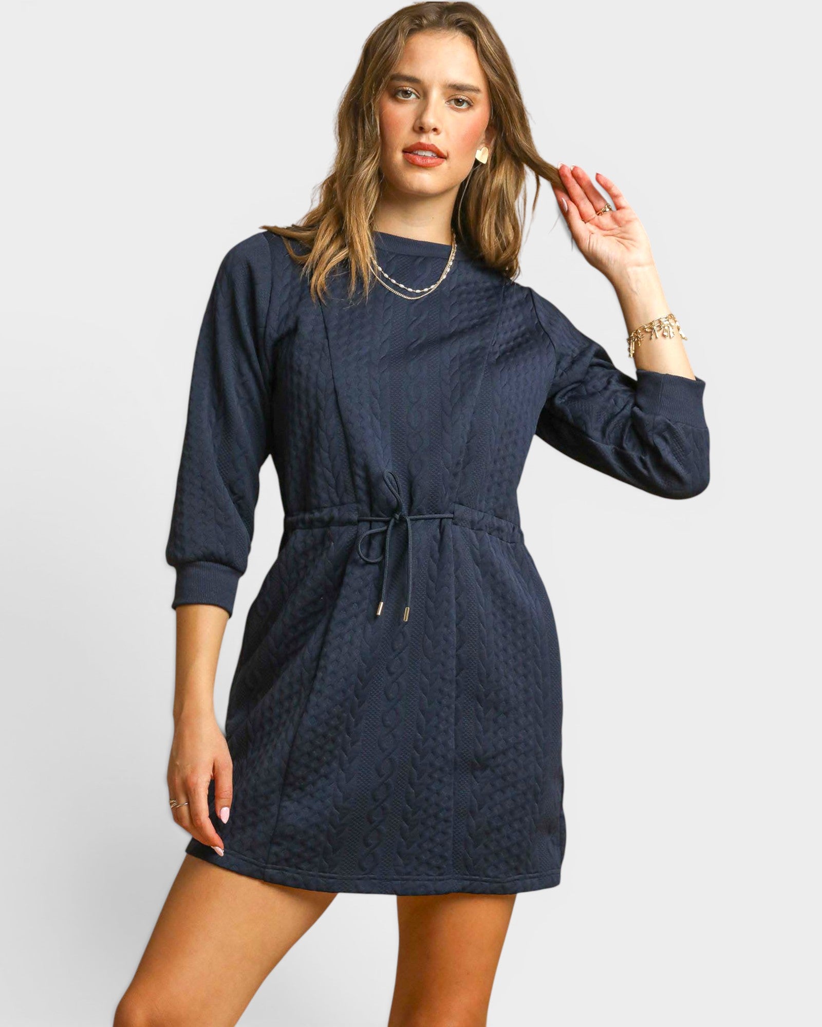 Woman wearing a navy blue dress with long sleeves on a light gray background