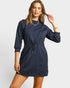 Woman wearing a navy blue dress with long sleeves on a light gray background