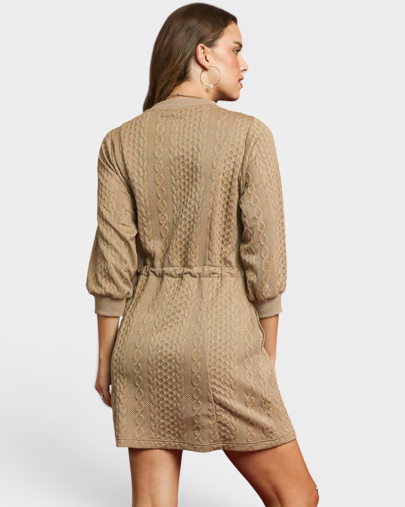 Woman wearing a beige cable knit dress on a plain background