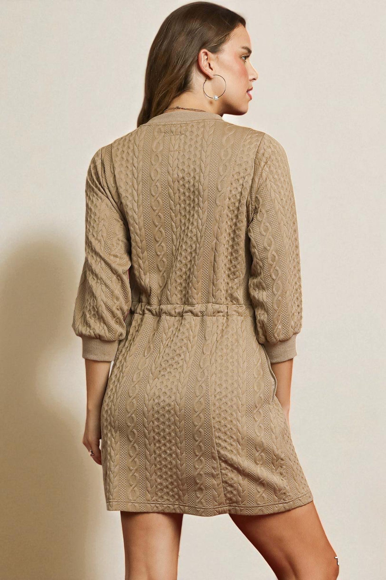 Woman wearing a beige cable knit dress against a plain background