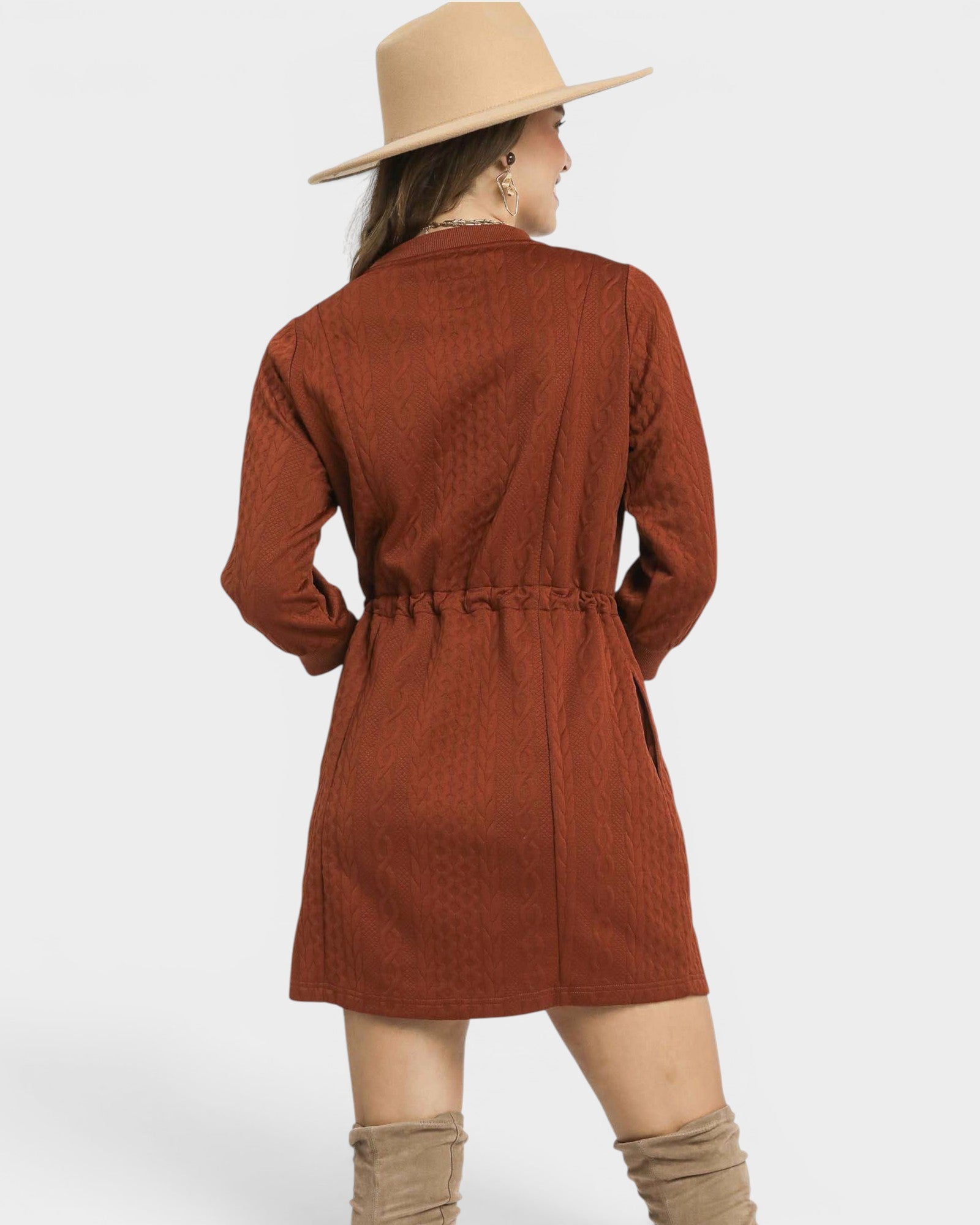 Person wearing a rust-colored dress with a belt and beige hat on a white background