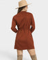Person wearing a rust-colored dress with a belt and beige hat on a white background