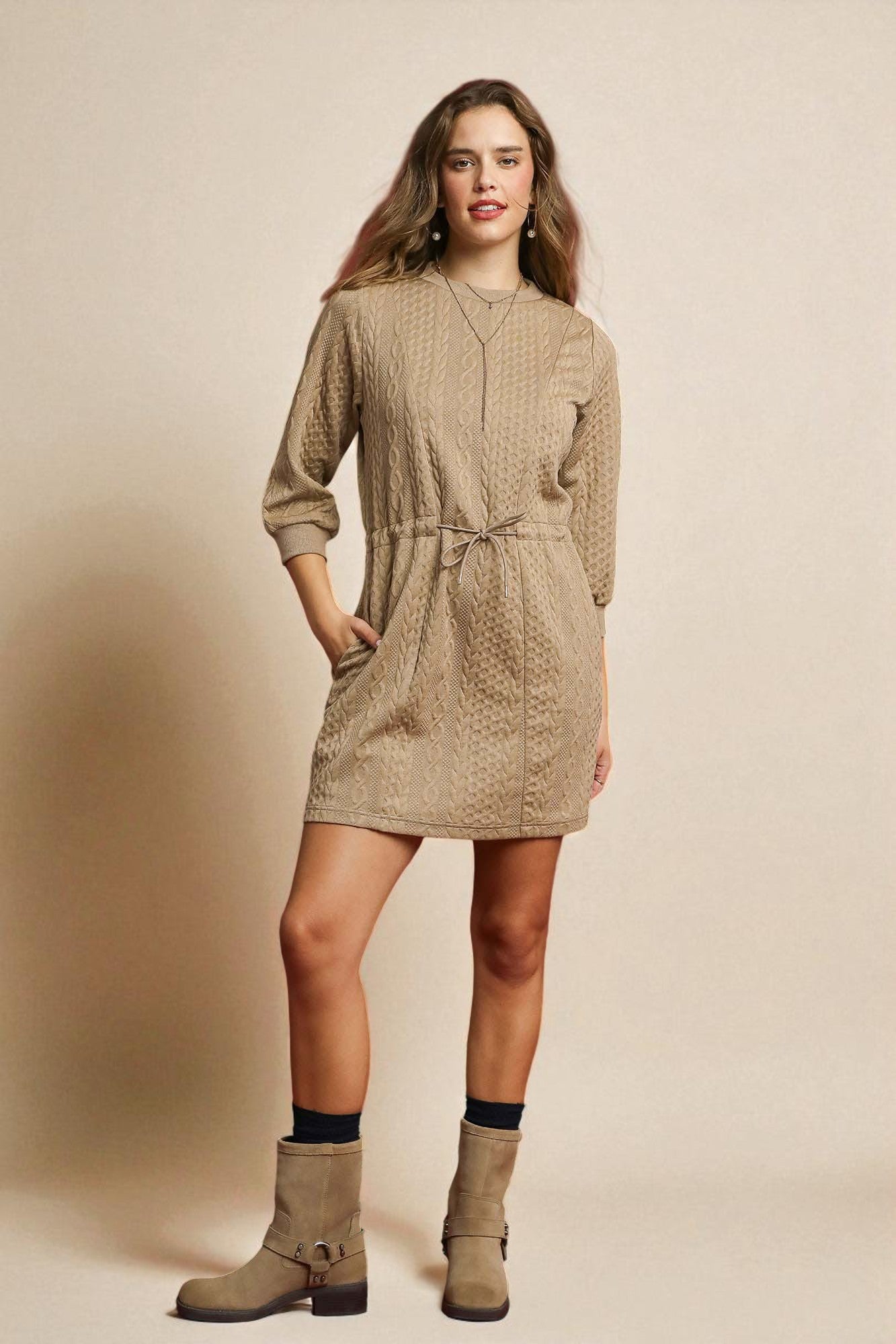 Woman wearing a beige patterned dress with matching boots against a beige background