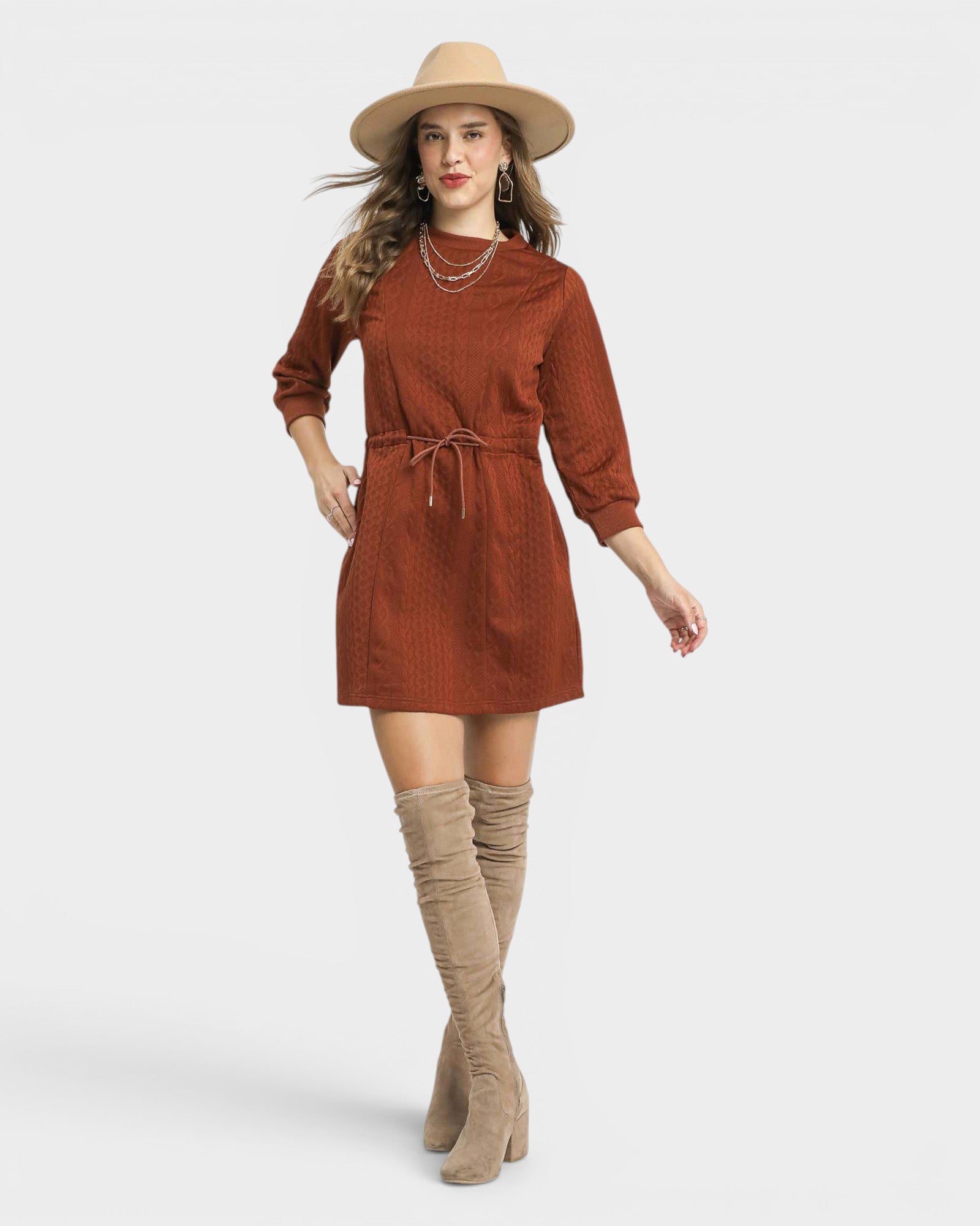 Woman wearing a brown dress with a hat and beige boots on a white background