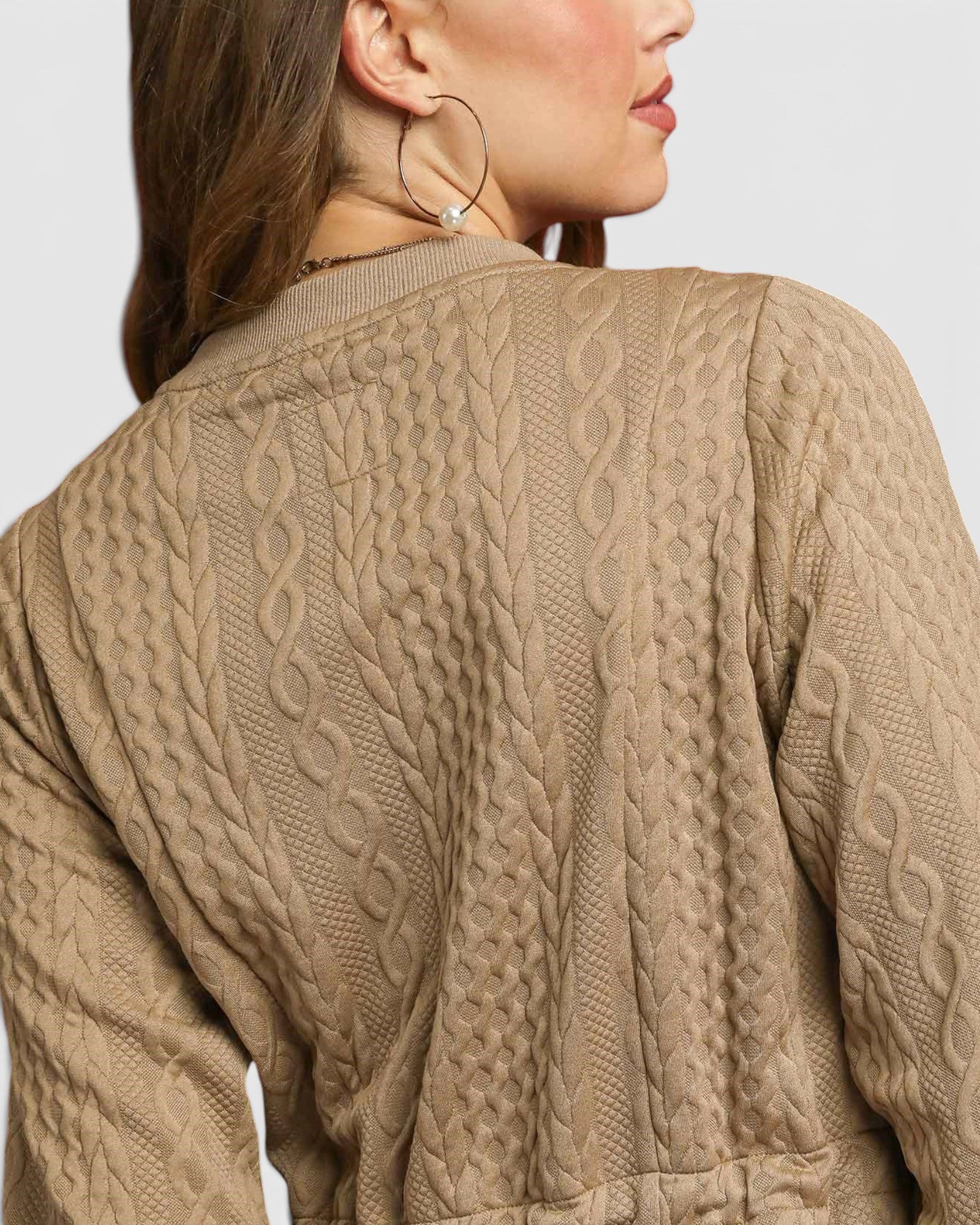 Close-up of a person wearing a beige cable knit sweater on a light gray background