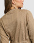 Close-up of a person wearing a beige cable knit sweater on a light gray background
