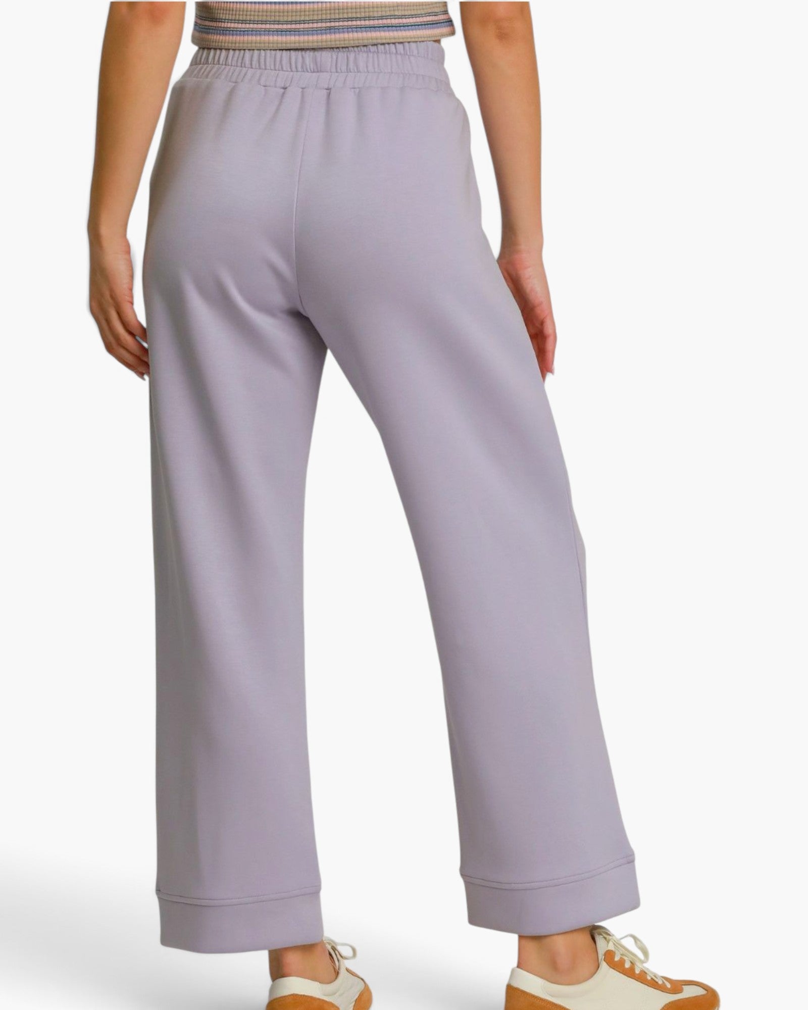 A person shown from the back wearing light lavender wide-leg cropped sweatpants with an elastic waistband and cuffed hems, paired with a striped top and white sneakers.