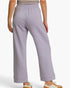 A person shown from the back wearing light lavender wide-leg cropped sweatpants with an elastic waistband and cuffed hems, paired with a striped top and white sneakers.