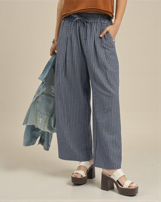 Person wearing blue striped pants with a brown top and denim jacket on a beige background