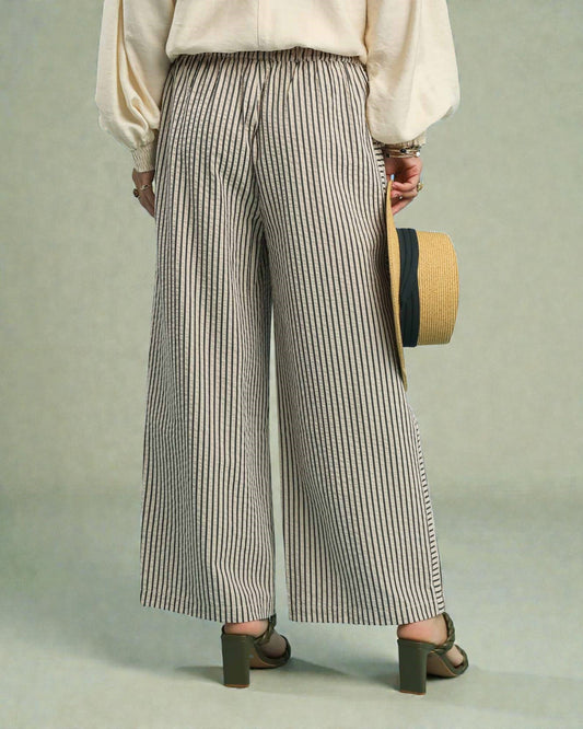 Person wearing wide-leg striped pants holding a hat against a plain background