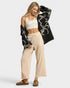Woman wearing a black patterned cardigan, white top, beige pants, and brown shoes on a white background