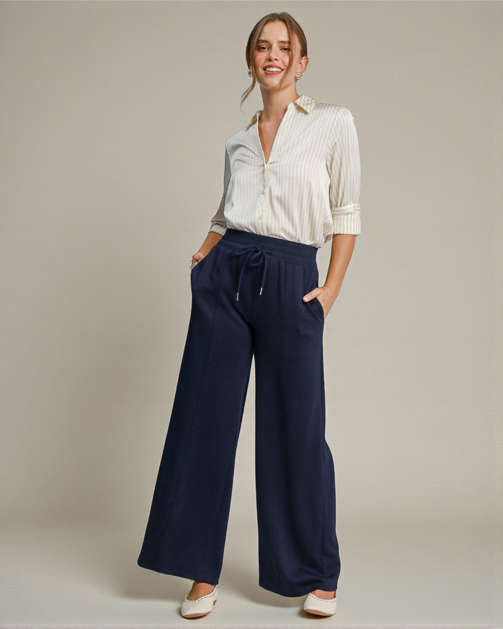 Woman wearing a white blouse and navy wide-leg pants against a plain background