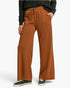 A person wearing rust-brown wide-leg drawstring pants, a black long-sleeve top, and black sneakers, shown from the waist down against a light gray studio background.